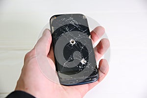 Man holding crashed black smartphone with a bullet hole in hand. Broken lcd touch screen. Information technology photo. War