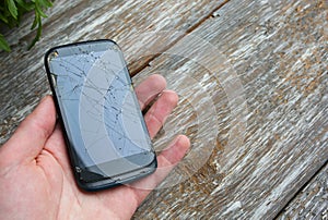 Man is holding a crashed black smartphone in hand on the wooden background. Broken lcd touch screen. Information technology photo