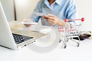 Man holding credit card in hand and entering security code using smart phone on laptop keyboard, online payment shopping concept