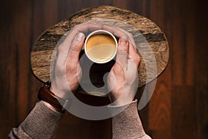 Man holding a cup of coffee on a wooden, vintage background. Hand of young businessman holding a mug of coffee. Vintage tones.