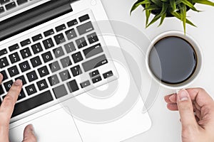 Man is holding a cup of coffee while working using laptop. Top view