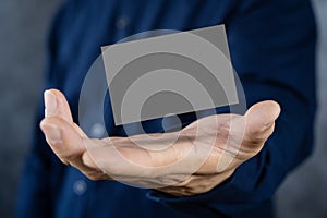 Man holding a dark gray business card against a concrete wall Mature male hand holding a blank business card in front of the