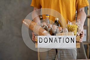 A man holding a donation box of different products on grey background, Volunteer with donations box with food