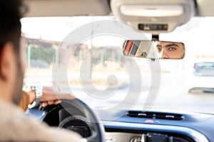 Man holding driving wheel riding car looking in rearview mirror at daytime