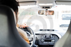 Man holding driving wheel riding car looking in rearview mirror at daytime