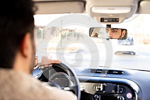 Man holding driving wheel riding car looking in rearview mirror at daytime