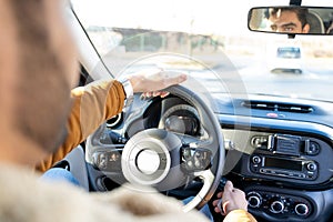 Man holding driving wheel riding car looking in rearview mirror at daytime