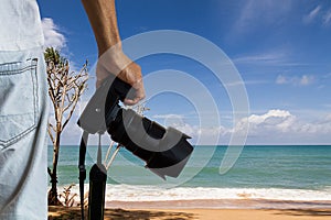 Man holding dslr digital camera on blurred beach and blue cloudy sky background