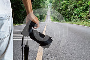 Man holding dslr digital camera on blurred straight road in national park background