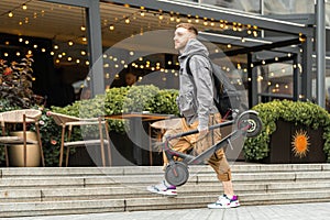 Man holding electric kick scooter while going for a walk at street or at cafe