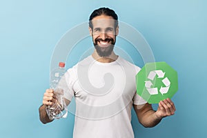 Man holding empty plastic bottle and green recycling sign, looking at camera.