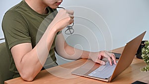 Man holding eyeglasses and working with laptop at home.