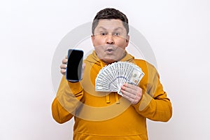 Man holding fan of dollar banknotes and smart phone with black blank screen, making money online.