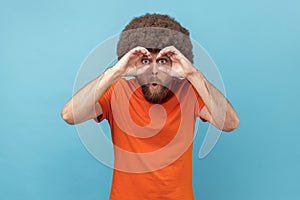 Man holding fists near eyes imagining binoculars and looking through holes, spying, having fun.