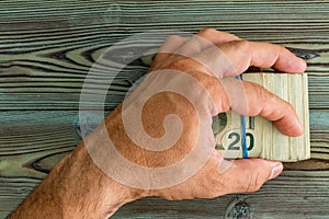 Man holding a folded wad of 20 dollar banknotes