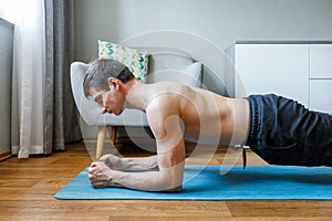 Man holding forearm plank pose doing yoga at home