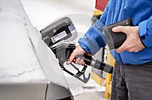 Man holding fuel nozzle, filling gas tank of diesel car covered with snow