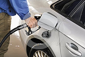 Man holding fuel nozzle, filling gas tank of diesel car covered with some rain drops