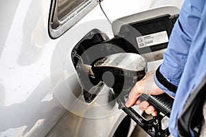 Man holding fuel nozzle, filling gas tank of diesel car covered with some rain drops