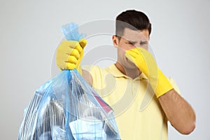 Man holding full garbage bag against light background, focus on hand