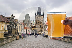 Man holding glass of light beer with view of Charles bridge in Prague