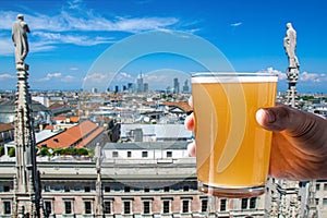Man holding glass of light beer with view from Milan Cathedral Duomo di Milano roof in Italy. Milan skyline with modern