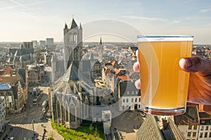 Man holding glass of light belgian beer against view of big cathedral in Ghent