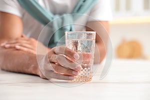 Man holding glass of pure water at table in kitchen, closeup