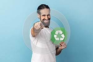 Man holding green recycling sign, pointing to camera, calls on to save our planet from pollution.