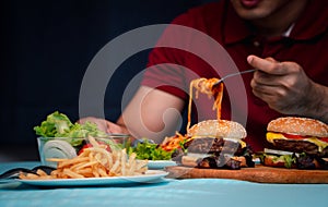Man holding hamburger on the wooden plate after delivery man delivers foods at home. Concept of binge eating disorder BED and photo