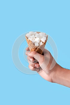 Man holding in hand ice-cream wafer cone filled with white sugar cubes isolated on blue background