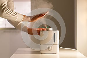 Man holding hand over steam aroma oil diffuser on the table at home, steam from the air humidifier