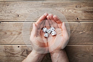 Man holding in hand white dice over the wooden table top view. Gambling devices. Game of chance concept.