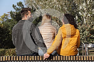 Man holding hands with another woman behind his girlfriend`s back on bench in park. Love triangle