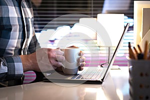 Man holding hands around coffee cup or tea mug in home office.