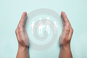 Man holding hands around cutout paper silhouette of family on light blue background, top view. Insurance concept