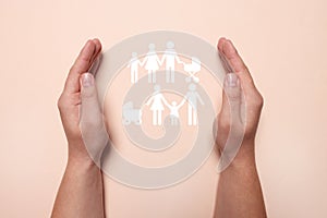 Man holding hands around cutout paper silhouette of family on pink background, top view. Insurance concept