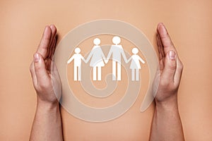 Man holding hands around paper silhouette of family on coral background, top view. Insurance concept