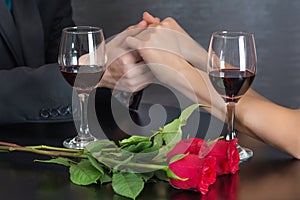 Man holding hands of girl on restaurant table with two red wine glasses and red roses flower