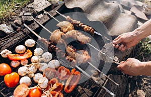 Man holding in hands grilled vegetables, chicken and pork meat on the open fire. Onions, mushrooms, tomatoes and red pepper on the