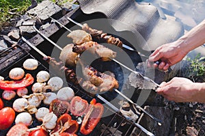 Man holding in hands grilled vegetables, chicken and pork meat on the open fire. Onions, mushrooms, tomatoes and red pepper on the