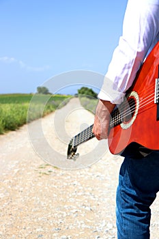 Man holding his classic guitar walking on the country road