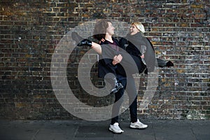 Man holding his girlfriend in his arms in front of a brick wall typical of London