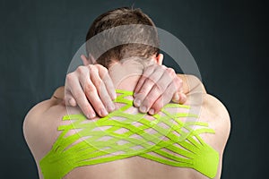 Man holding his neck with kinesiology medical tape applied to relieve back pain