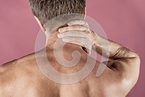 Man holding his neck in pain, on pink background. Lower neck pain. Shirtless man touching his neck for the pain