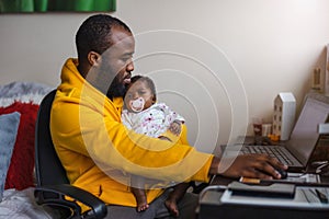 Man holding his newborn baby girl and working with laptop