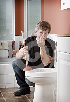 Man holding his nose holding a plunger by a toilet.
