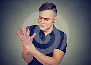 Man holding his painful wrist isolated on gray wall background. Sprain pain