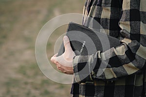 Man is holding the holy Bible outside on a blurred green background.