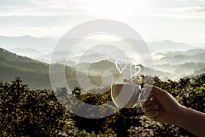 Man holding hot coffee cup forest and mountain backdrop foggy morning heart-shaped steam